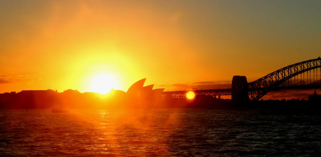 Toàn cảnh biểu tượng Nhà hát Con Sò Sydney Opera House soi bóng xuống mặt vịnh trong ánh hoàng hôn rực rỡ