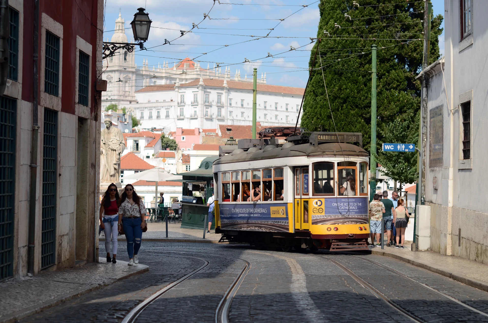 Chiếc xe điện màu vàng cổ kính tuyến Tram 28 di chuyển qua các con dốc lát đá khu phố cổ Alfama tại Lisbon