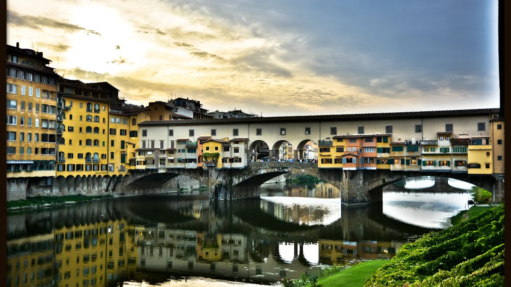 Cây cầu vòm đá Ponte Vecchio với những ngôi nhà cổ sơn vàng san sát soi bóng xuống dòng sông Arno lúc hoàng hôn