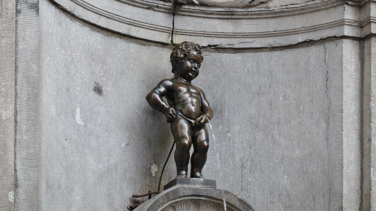 Bức tượng đồng nhỏ nhắn Manneken Pis đứng trên bệ đá đài phun nước cổ kính tại góc phố Brussels